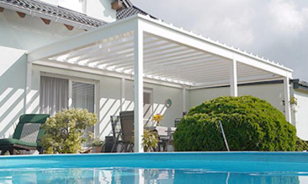 Terrassendach mit Drehlamellen an Hauswand und vor einem Pool